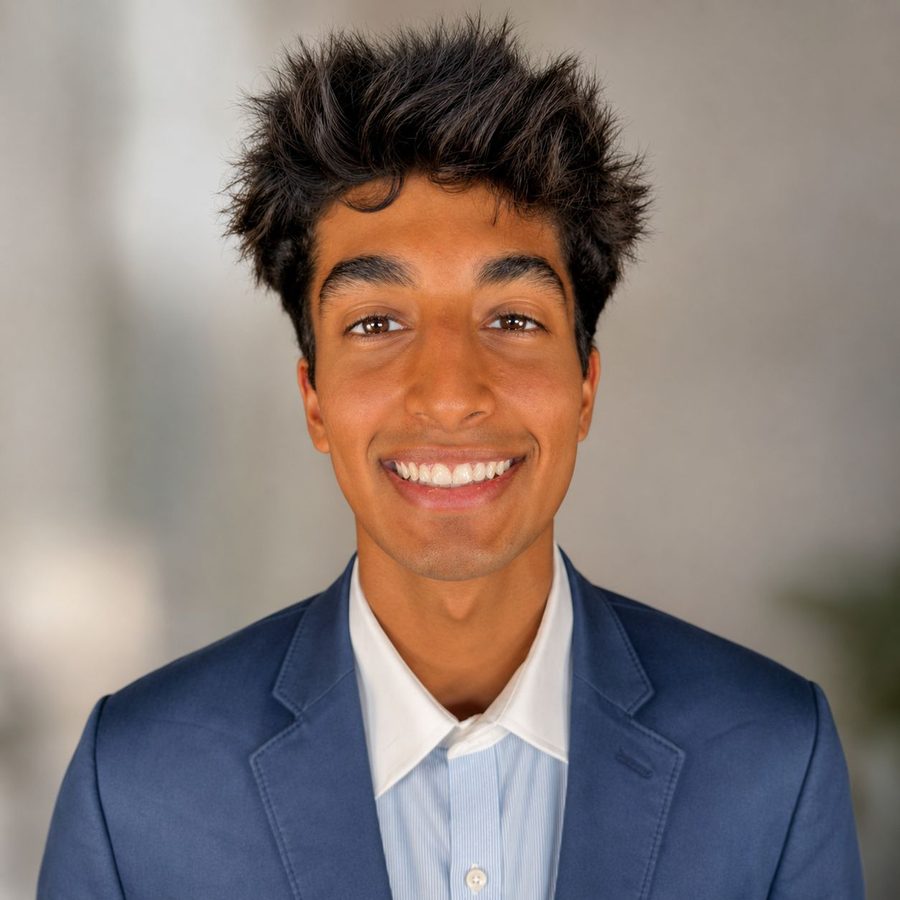 Portrait of Vedant Rai, smiling, in a navy blazer over a light blue striped shirt.